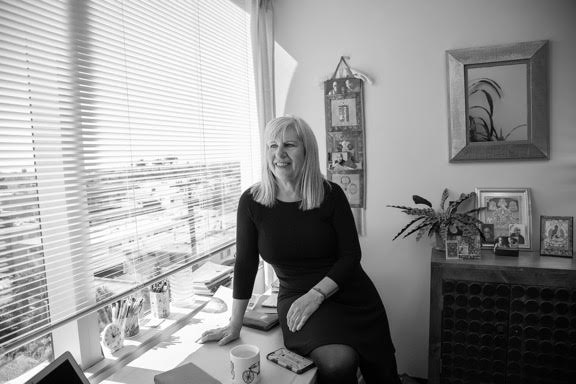 Judy sitting on her desk at the office facing the camera but looking out her office window.